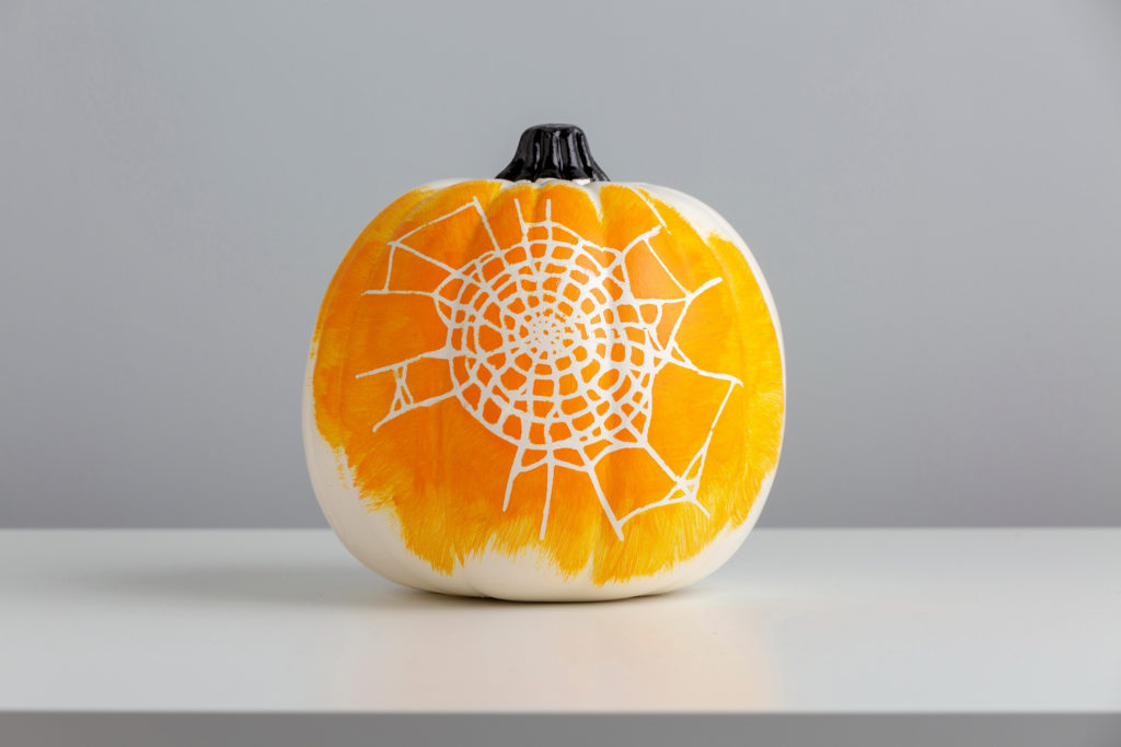 Orange and white spider web painted on white pumpkin with stencil
