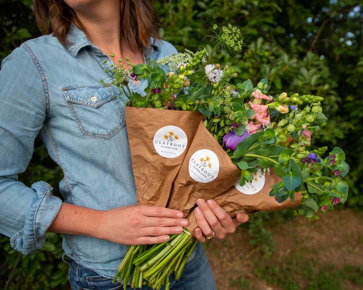 Person holding bouquets of spring flowers from Clayroot Flower Farm in Colorado with paper wrapping decorated with Cricut made label