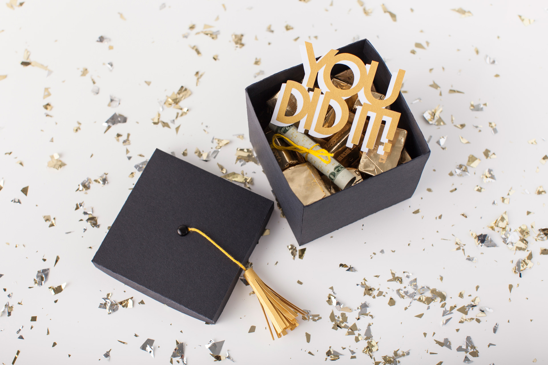 Black graduation cap-shaped gift box stuffed with chocolates and money and Cricut-cut sign that says "You Did It"