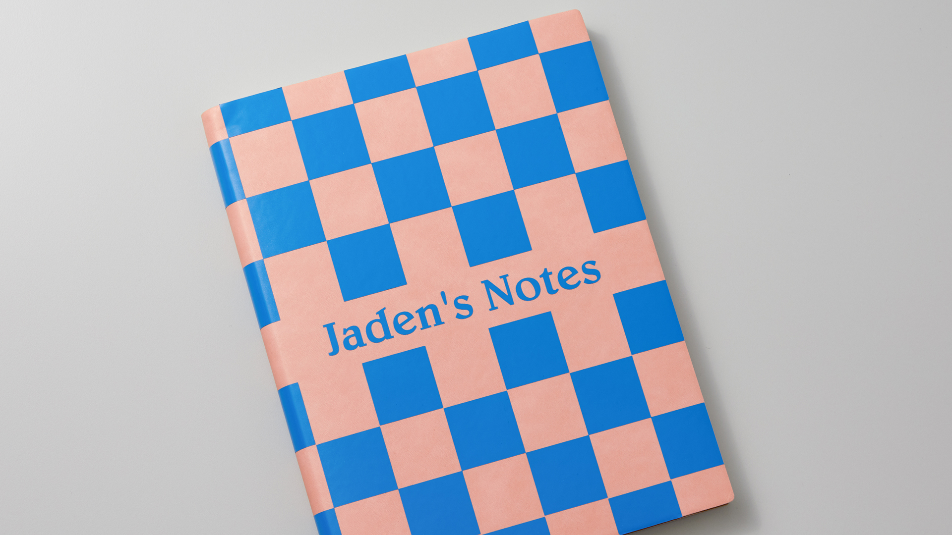 Personalized pink notebook with blue checkered design and "Jaden's Notes" across the middle of the book cover.