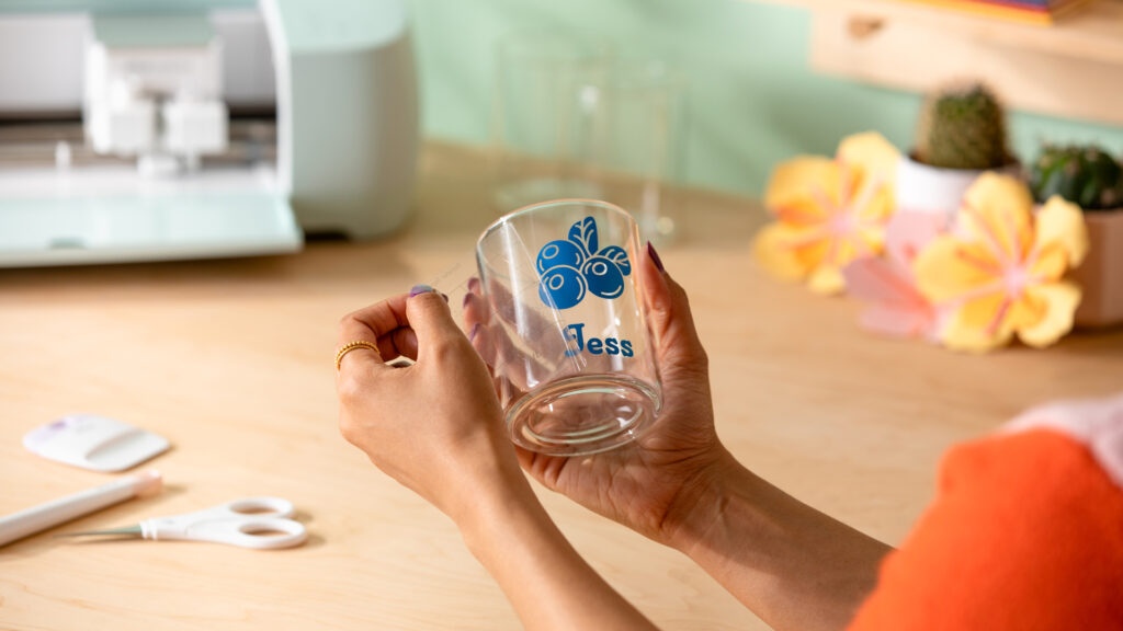 Person holding a glass personalized with the name Jess and an image of blueberries, peeling off a piece of transfer tape