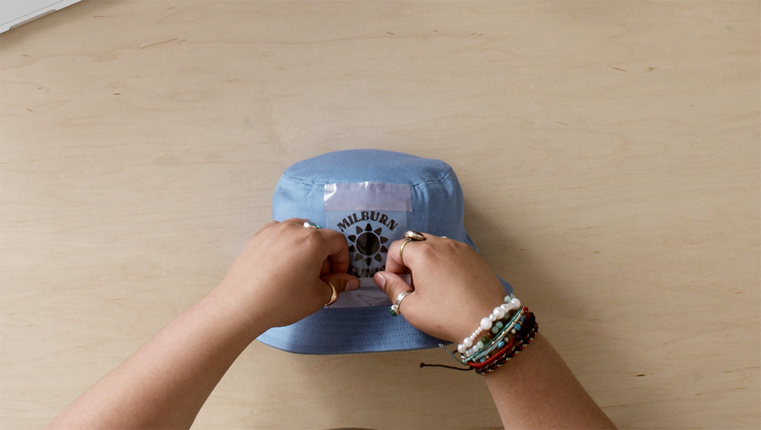 taping down iron-on family reunion design to blue bucket hat
