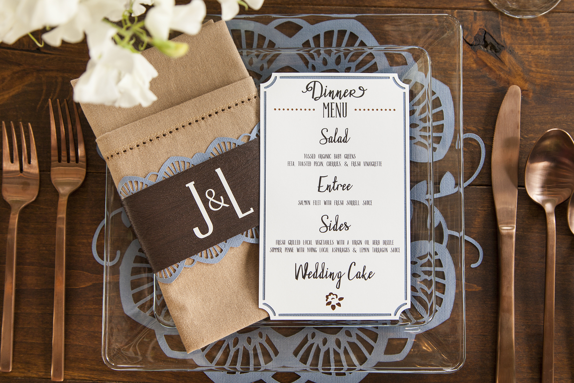 Wedding dinner menu on a clear plate with a lace cutout design on cardstock underneath