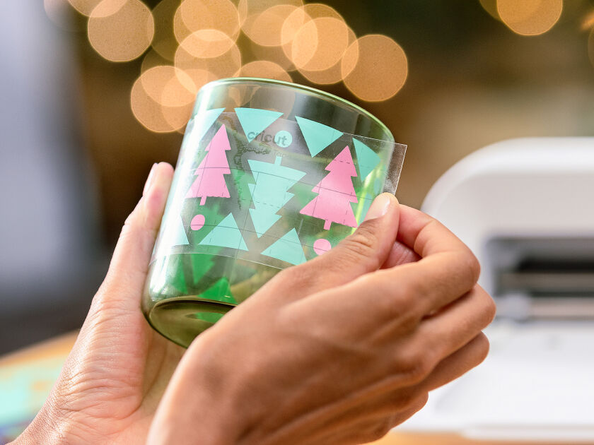 Woman's hands using transfer tape to adhere the blue vinyl onto a small drinking glass
